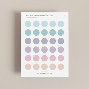 May include: A sheet of pastel colored dot stickers. The sticker sheet has the text "Minimal Dots - Pastel Dreams" and "Matt Sticker Sheet" printed on it. The dots are arranged in rows of five, with the colors transitioning from light blue to purple to pink to beige.
