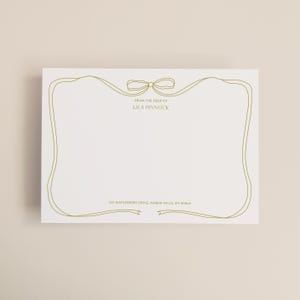 May include: A white stationery card with a gold ribbon design and a bow at the top. The text "FROM THE DESK OF LILA PINNOCK" is printed at the top, with an address at the bottom.
