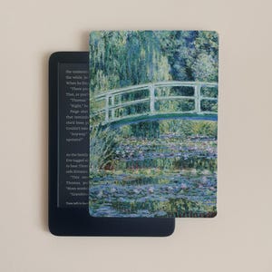 May include: A Kindle e-reader with a cover featuring a painting of a green arched bridge over a pond with water lilies. The painting has a soft, impressionistic style with green and blue hues.