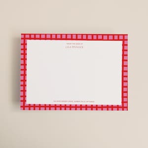 May include: A rectangular stationery card with a red and pink checkered border. The card has the text "FROM THE DESK OF LILA PINNOCK" and the address "742 MAPLEBERRY DRIVE, AMBER FALLS, WY 82845" printed on it.