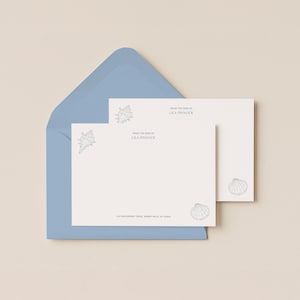 May include: A stationery set with a pale blue envelope and cream-coloured notecards. The cards and envelope feature seashell illustrations. Text on the cards reads "From the desk of Lila Pinnock" and the address. Stationery for letters.