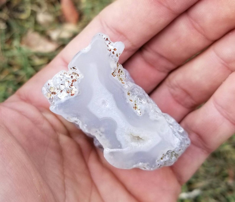 Puede incluir: Una geoda de &aacute;gata azul claro con inclusiones marrones y blancas. La geoda es lisa y tiene una forma natural irregular.