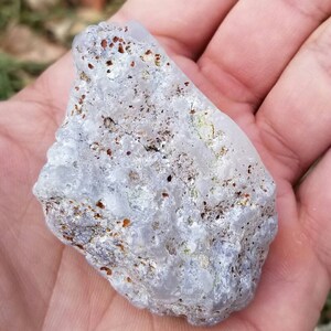 Puede incluir: Una roca blanca transl&uacute;cida con motas marrones y plateadas. La roca tiene una superficie rugosa y desigual.