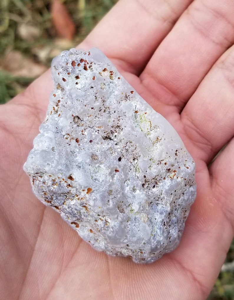 Puede incluir: Una roca blanca transl&uacute;cida con motas marrones y plateadas. La roca tiene una superficie rugosa y desigual.