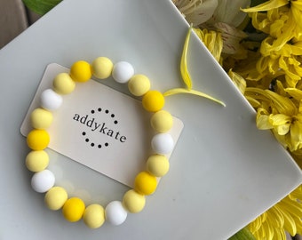 May include: A yellow and white beaded bracelet with the text "addykate" on a white card.
