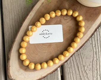 May include: A gold beaded bracelet with a textured surface. The bracelet is on a wooden surface with a white card that says "addykate" in black text.