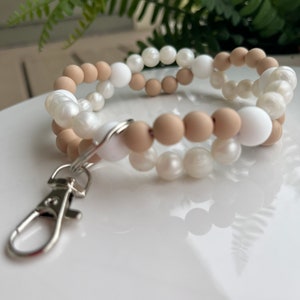 May include: A white and beige beaded keychain with a silver clip. The beads are round and have a smooth, polished finish.