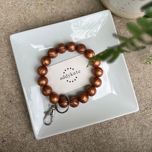 May include: A copper-colored silicone beaded keychain with a silver key ring and a small card that says "addykate" with a circle pattern.