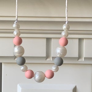 May include: A necklace made of white, gray, and pink beads. The beads are strung on a white cord.
