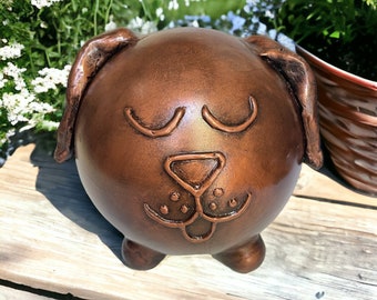 May include: A brown ceramic dog figurine with a round body and a cute face. The dog has closed eyes and a small, detailed nose and mouth.