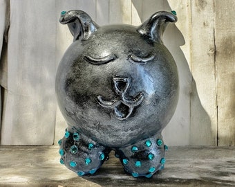 May include: A black ceramic piggy bank with a cute face and turquoise rhinestones on its feet.