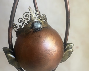May include: A copper-colored orb with a gold crown and a light blue gemstone sits on a decorative metal stand with a vine-like design.