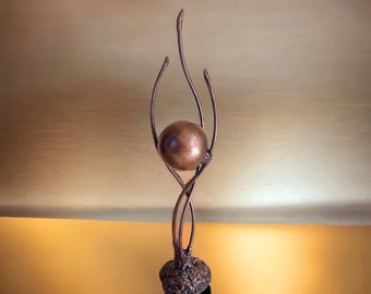 May include: A copper sculpture of a sphere held aloft by a stylized, abstract, branching form.