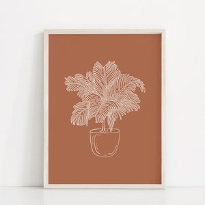 May include: A white line drawing of a potted palm tree on a terracotta background. The image is framed in a white frame.