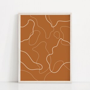 Puede incluir: Una impresión enmarcada con un diseño abstracto minimalista. La impresión presenta líneas blancas que forman formas orgánicas sobre un fondo naranja quemado.