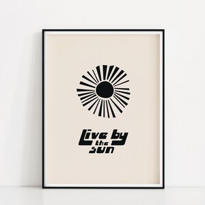 Puede incluir: Impresi&oacute;n en blanco y negro con un dise&ntilde;o de sol estilizado y el texto "Live by the sun" sobre un fondo beige.
