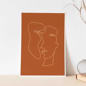 May include: Abstract line art print of two faces in a minimalist style on a burnt orange background.
