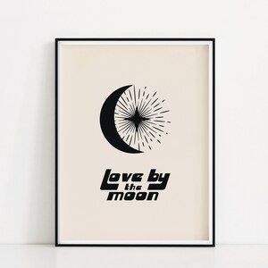 Puede incluir: Impresi&oacute;n en blanco y negro con una luna creciente y un dise&ntilde;o de estallido de estrellas. El texto "Love by the moon" est&aacute; impreso debajo del dise&ntilde;o. La impresi&oacute;n est&aacute; enmarcada en un marco negro.