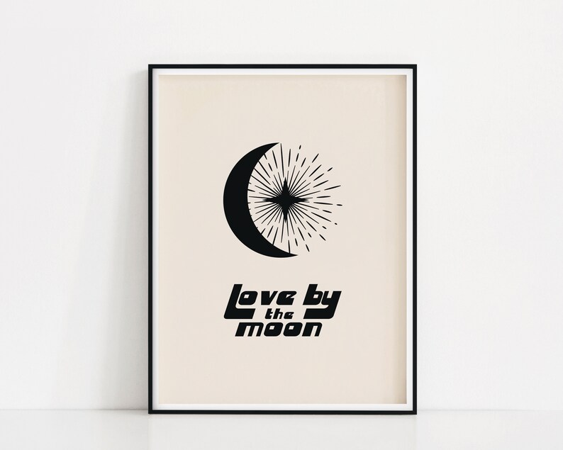 Puede incluir: Impresi&oacute;n en blanco y negro con una luna creciente y un dise&ntilde;o de estallido de estrellas. El texto "Love by the moon" est&aacute; impreso debajo del dise&ntilde;o. La impresi&oacute;n est&aacute; enmarcada en un marco negro.