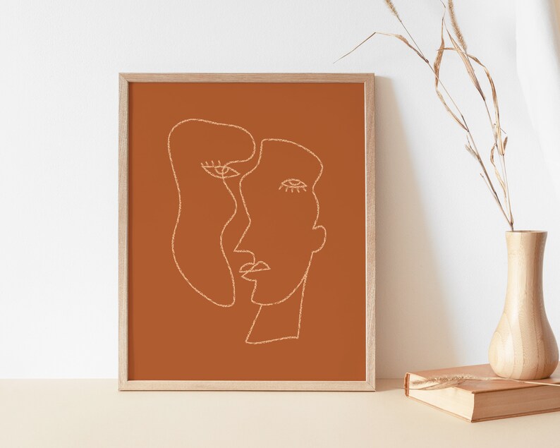 May include: A framed print with a minimalist line drawing of two faces in white on a burnt orange background.