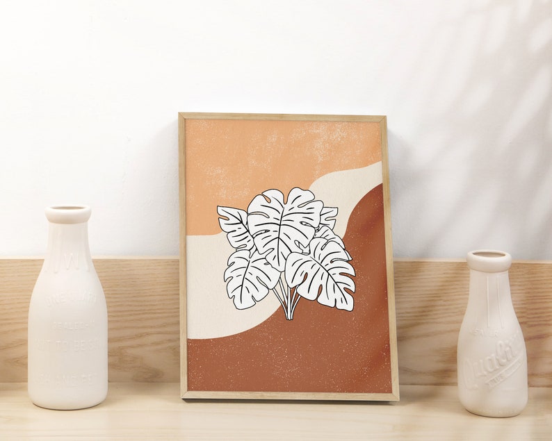 May include: A framed print with a minimalist design featuring a white outline of tropical leaves on a background of orange, brown, and cream.