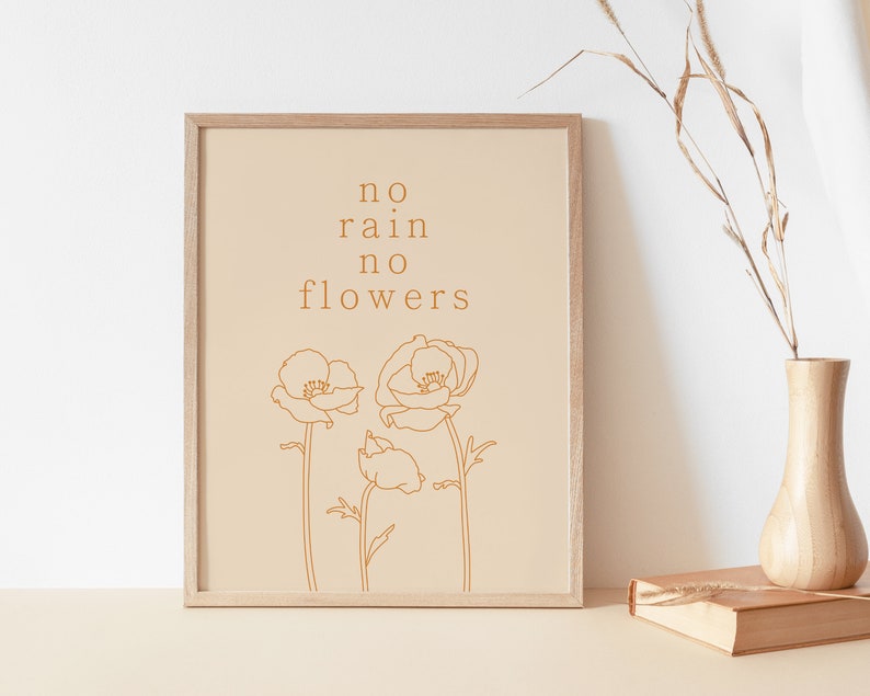 May include: A beige framed print with the text "no rain no flowers" in brown text. The print features a line drawing of three orange flowers.