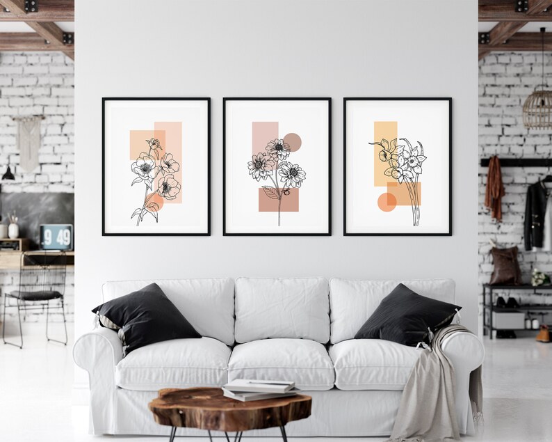 May include: Three minimalist line art prints of flowers with geometric shapes in peach and orange tones. The prints are framed in black and hung on a white wall.