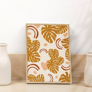 May include: A framed print with a white background and a pattern of brown leaves and pink shapes. The leaves are stylized and resemble monstera leaves.