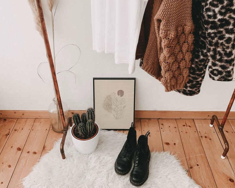 May include: A white, fluffy rug with two black leather boots on top. The boots have laces and are in a rustic setting with a wooden floor and a copper pipe rack in the background.