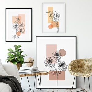 May include: Three minimalist art prints featuring black line drawings of flowers with abstract geometric shapes in peach and orange tones. The prints are framed in black and hung on a white wall.