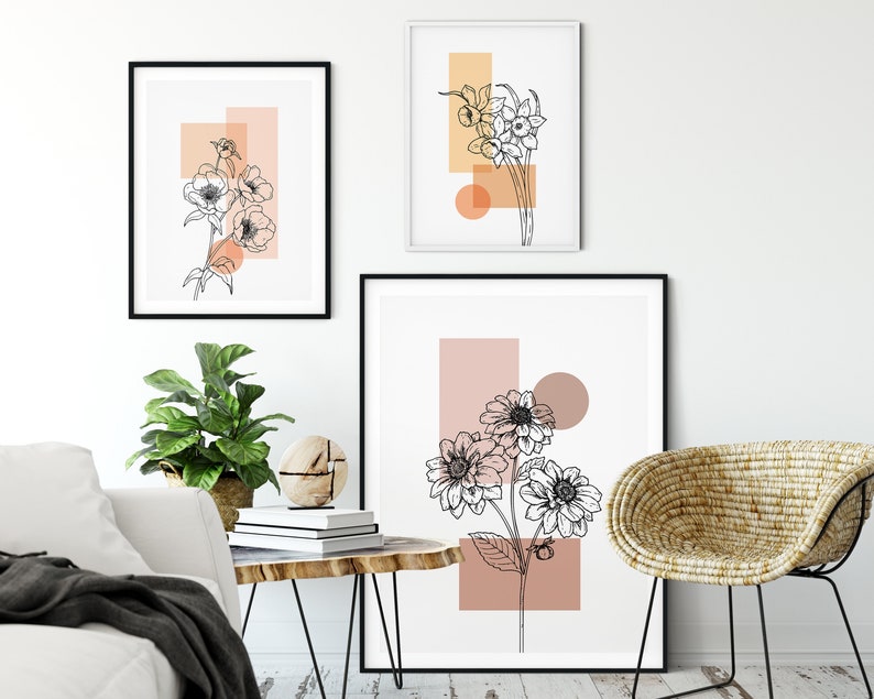 May include: Three minimalist art prints featuring black line drawings of flowers with abstract geometric shapes in peach and orange tones. The prints are framed in black and hung on a white wall.