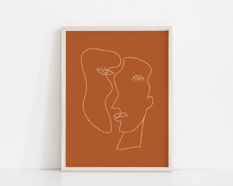 May include: A minimalist line art print of two faces in a continuous line, set against a burnt orange background. The print is framed in a white frame.