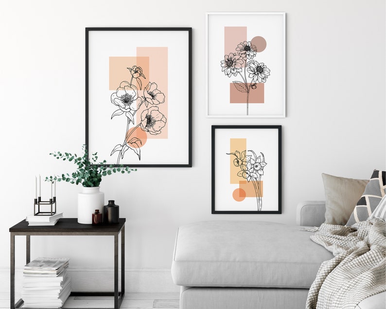 May include: Three black framed prints with white line drawings of flowers on a peach background. The prints are hung on a white wall.