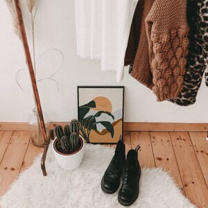 May include: A white faux fur rug with two black leather boots on top. The boots have laces and are in a rustic setting with a wooden floor and a copper pipe rack in the background.