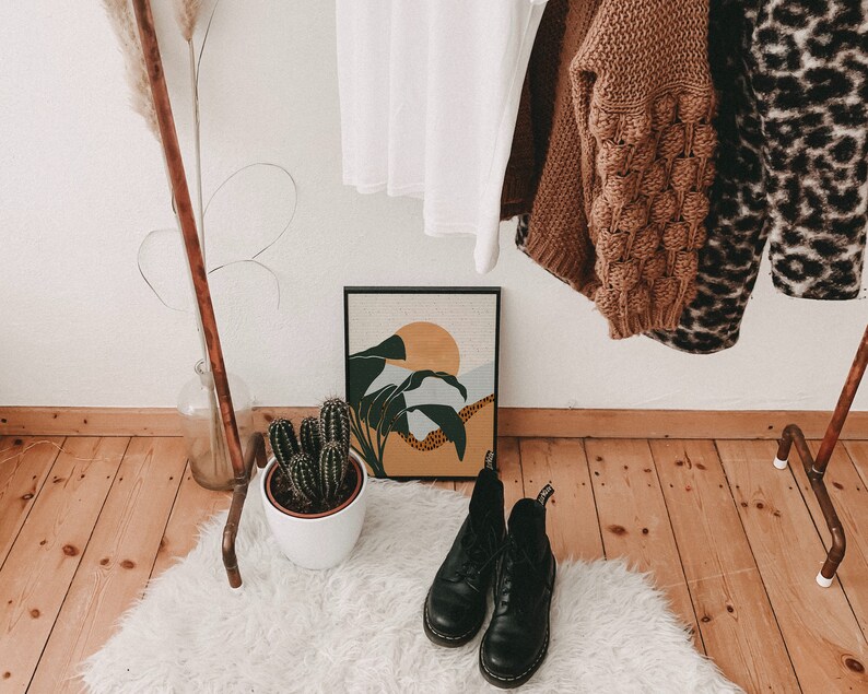 May include: A white faux fur rug with two black leather boots on top. The boots have laces and are in a rustic setting with a wooden floor and a copper pipe rack in the background.