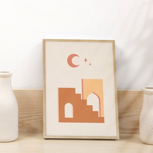 May include: A framed print with a minimalist design featuring a crescent moon and stars above a stylized building with a dome. The building is in shades of orange and brown against a cream background.