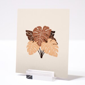 May include: A beige card with a brown and orange illustration of tropical leaves. The leaves are stylized and have a simple, modern design.