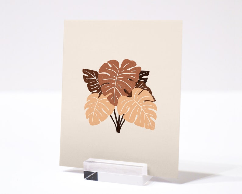 May include: A beige card with a brown and orange illustration of tropical leaves. The leaves are stylized and have a simple, modern design.