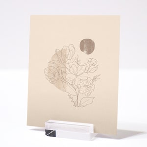 May include: A beige card with a line drawing of a bouquet of flowers in a circle with a brown circle behind it. The card is on a white surface.