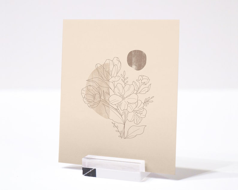 May include: A beige card with a line drawing of a bouquet of flowers in a circle with a brown circle behind it. The card is on a white surface.