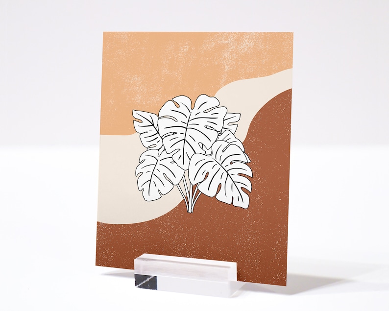 May include: A printable art print featuring a minimalist design of white monstera leaves on a background of brown and orange.