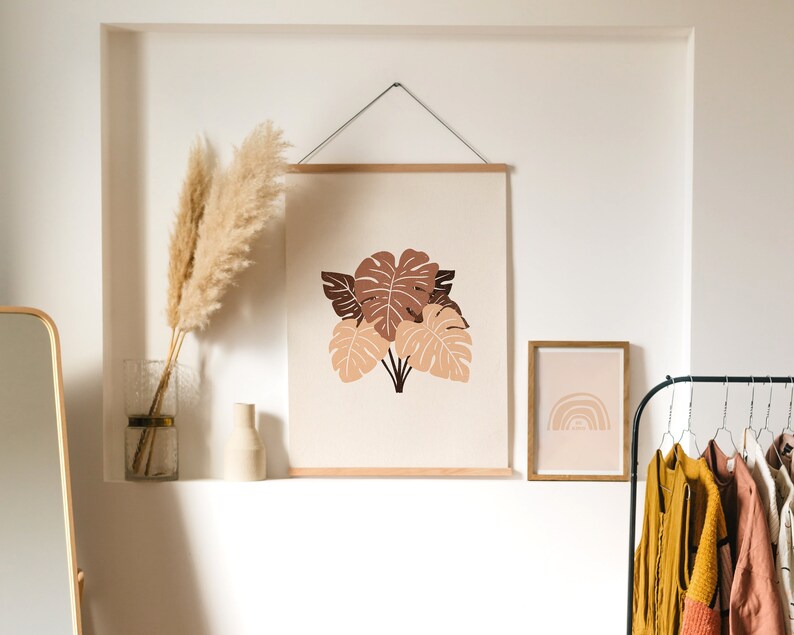 May include: A framed print with a minimalist design of brown and beige leaves on a cream background. A smaller framed print with a rainbow design is on the right. A vase with dried pampas grass is on a shelf below the prints.