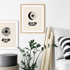 Puede incluir: Dos impresiones minimalistas en blanco y negro con un dise&ntilde;o de sol y luna. La impresi&oacute;n del sol dice "Live by the sun" y la impresi&oacute;n de la luna dice "Love by the moon".