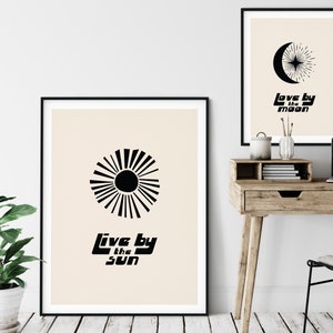 Puede incluir: Dos impresiones de arte minimalistas en blanco y negro con un dise&ntilde;o de sol y luna. La impresi&oacute;n del sol dice "Live by the sun" y la impresi&oacute;n de la luna dice "Love by the moon".