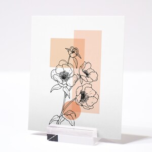 May include: A black and white line drawing of flowers with peach colored geometric shapes behind them. The image is printed on a white card.