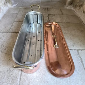 Puede incluir: Un calientaplatos antiguo de cobre y metal plateado abierto, con tapa. El interior tiene una base de metal perforada. La tapa tiene un asa de lat&oacute;n. El calientaplatos tiene un asa de lat&oacute;n en la parte superior y lateral.