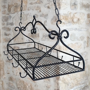 Peut inclure: Une étagère suspendue en métal noir dotée d'un plateau rectangulaire en fil de fer avec une base en grille. L'étagère est suspendue par deux chaînes métalliques fixées à des supports arqués décoratifs avec des volutes. Plusieurs petits crochets.