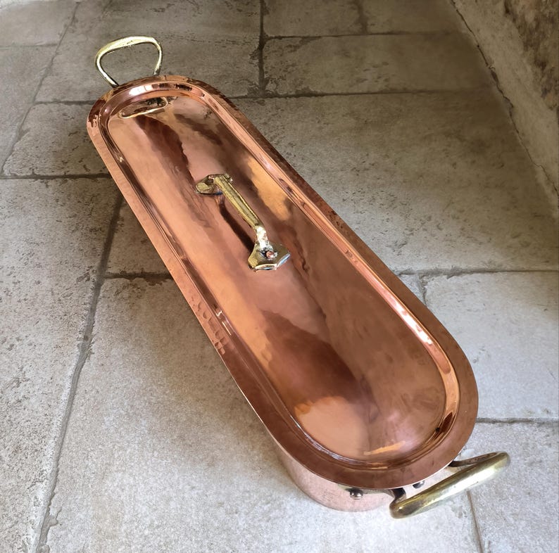 Puede incluir: Una ba&ntilde;era de cobre con asas de lat&oacute;n. La ba&ntilde;era tiene forma ovalada alargada con bordes redondeados. El interior es de cobre brillante, el exterior de un tono m&aacute;s oscuro. Las asas est&aacute;n en los laterales y en un extremo. Mide unos 150 cm de largo.