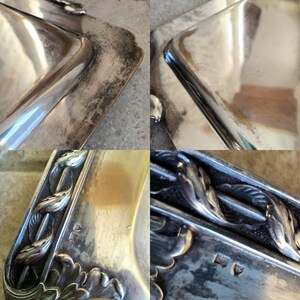 May include: A silver serving tray with ornate floral designs around the edge. The tray has a slightly tarnished finish and a hallmark on the bottom.
