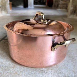 Peut inclure: Une casserole en cuivre avec une poignée et un couvercle en laiton. La casserole a une finition brillante et polie et est marquée "Fabriqué en France".